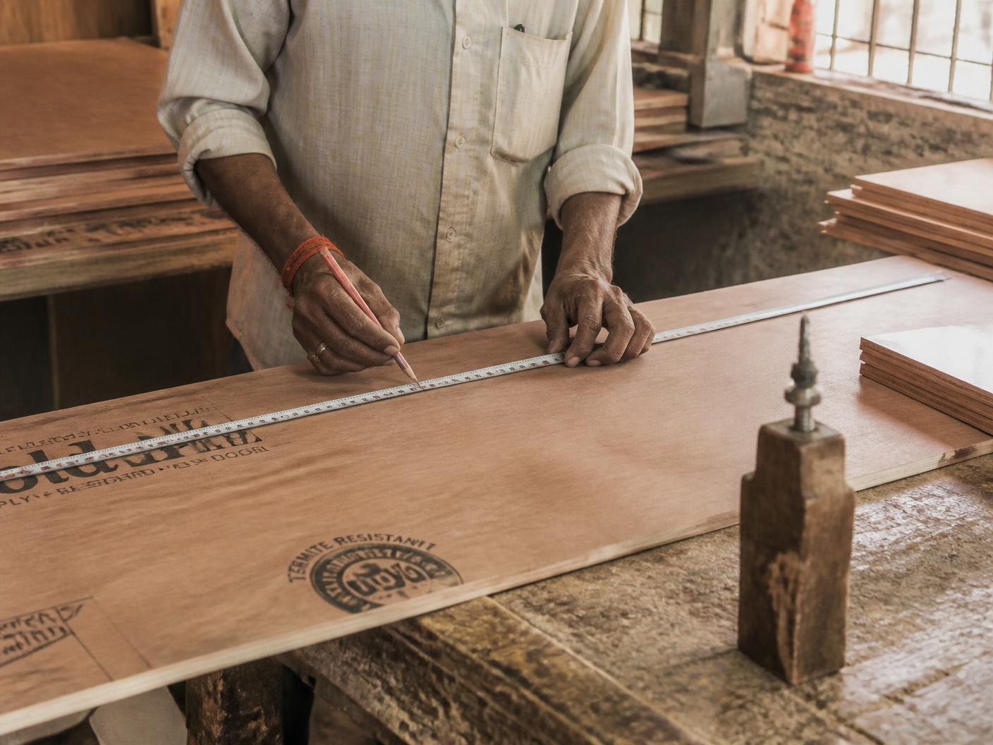 A carpenter measuring and marking a plywood sheet